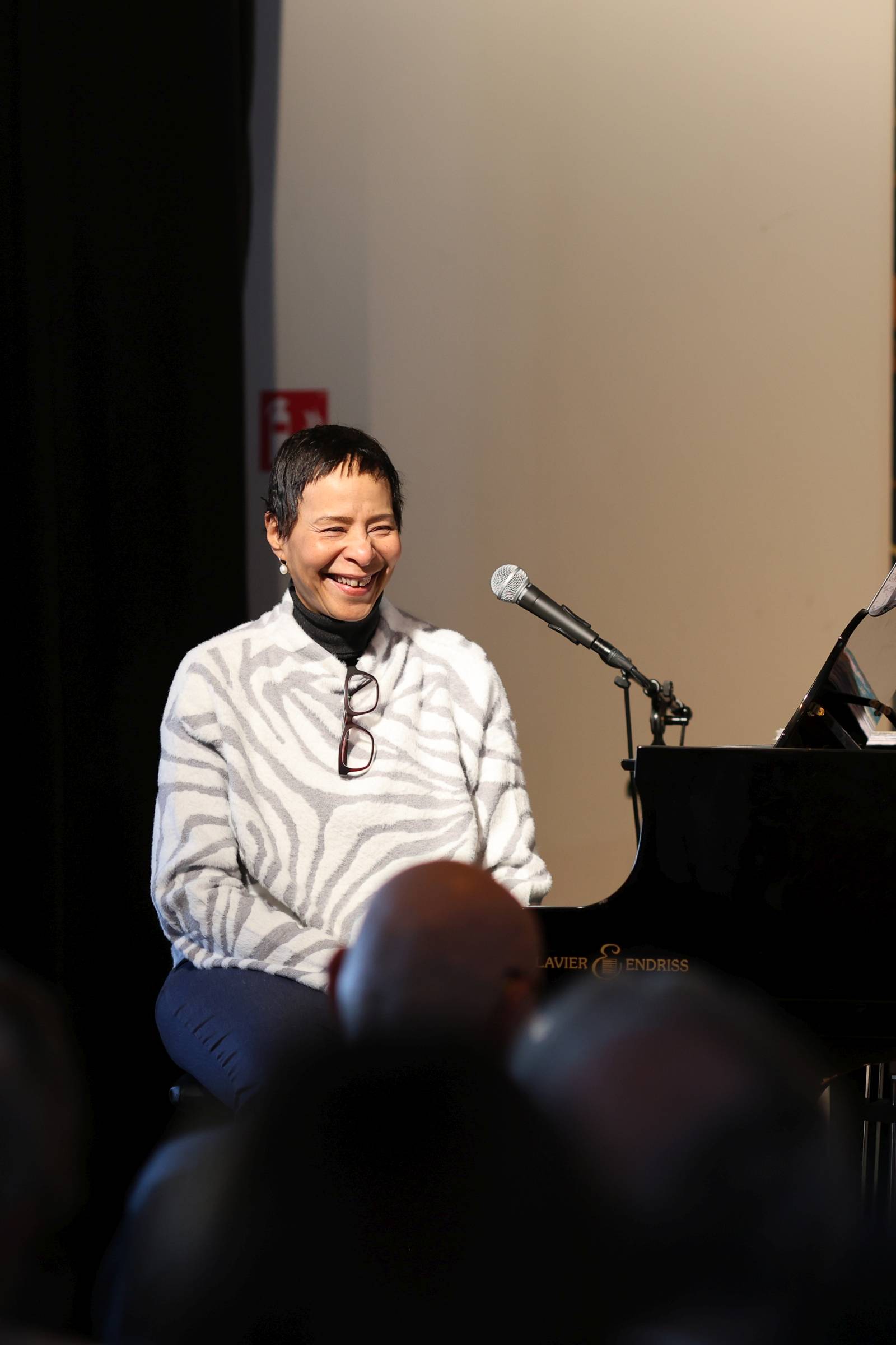 Sängerin Jocelyn B. Smith sitzt mit weiß-schwarz gemustertem Pullover an einem Flügel auf einer Bühne